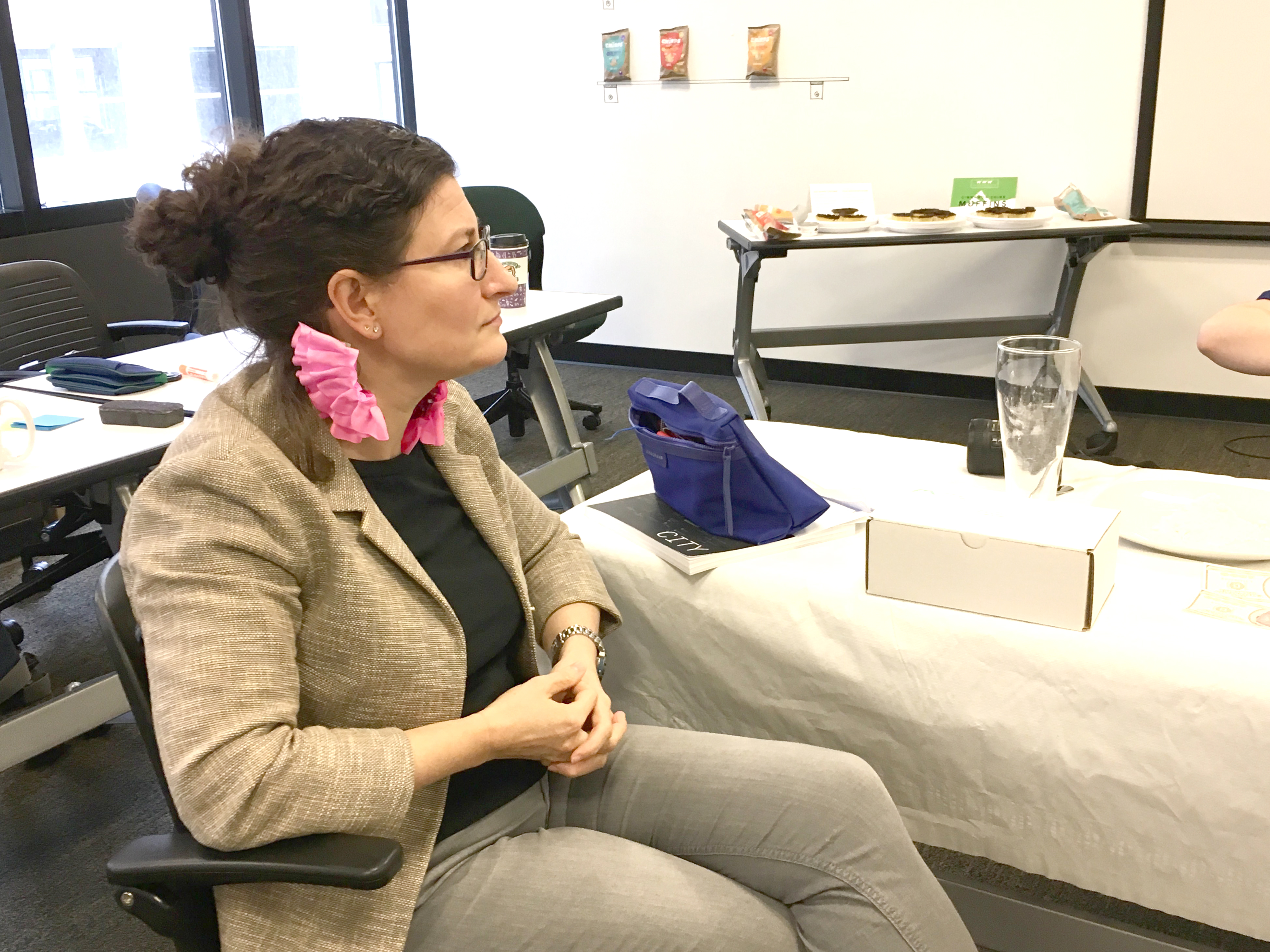 A woman sits in discussion in a classroom and wears pink frilly gills on her neck.